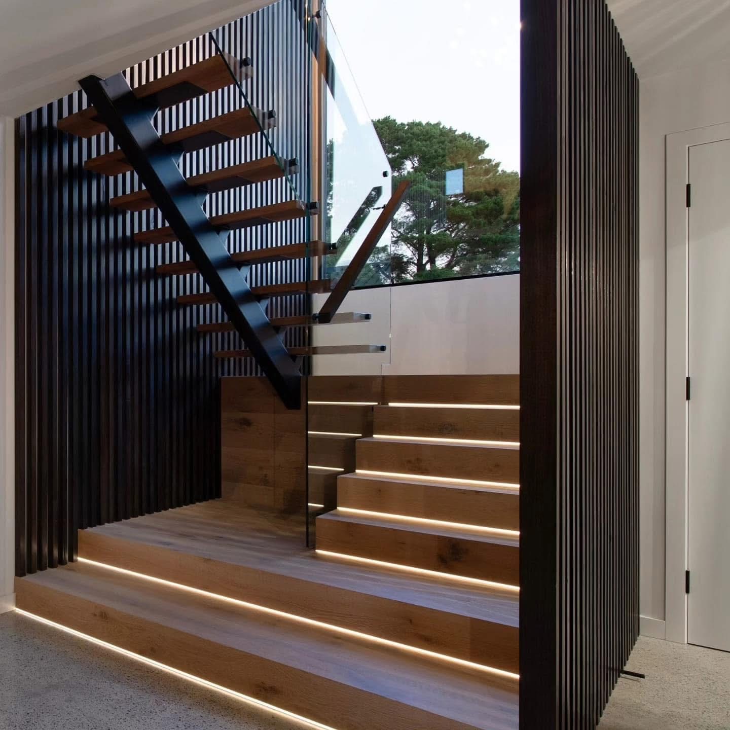 Clear glass balustrade beside timber stairs with warm step lighting