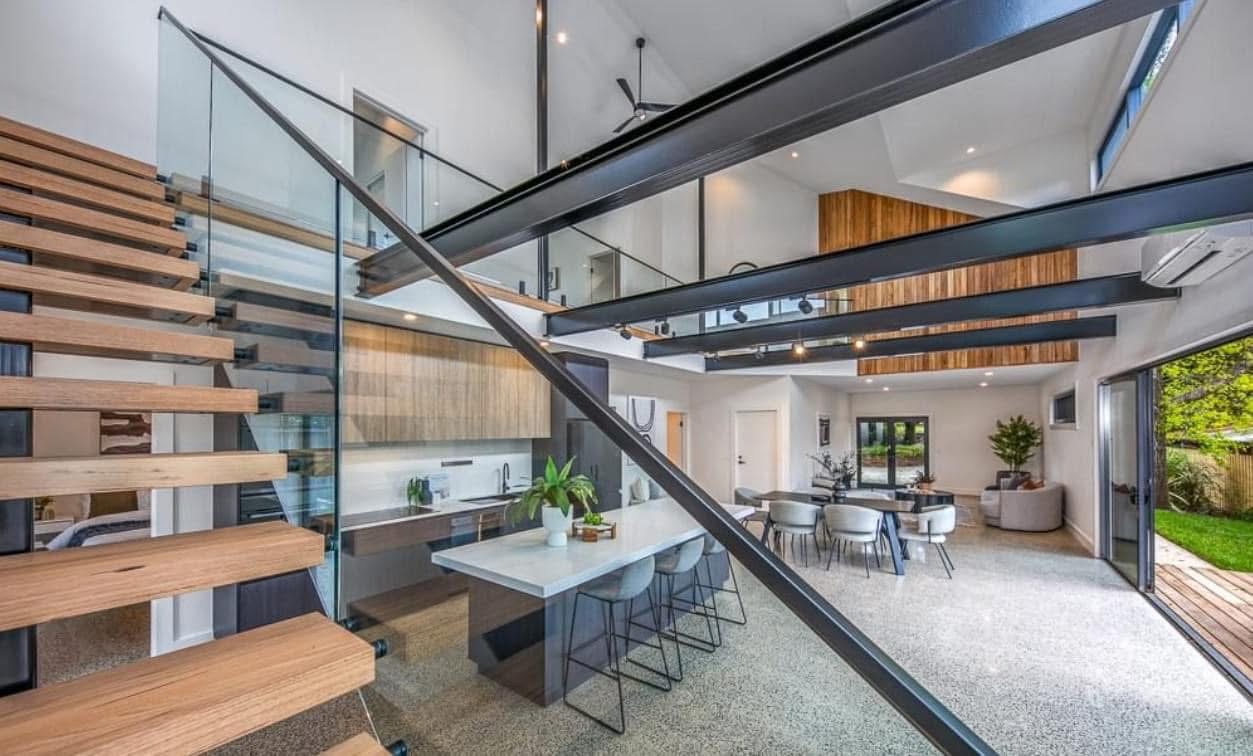 Glass balustrades around timber stairs and an upper landing above an open living space