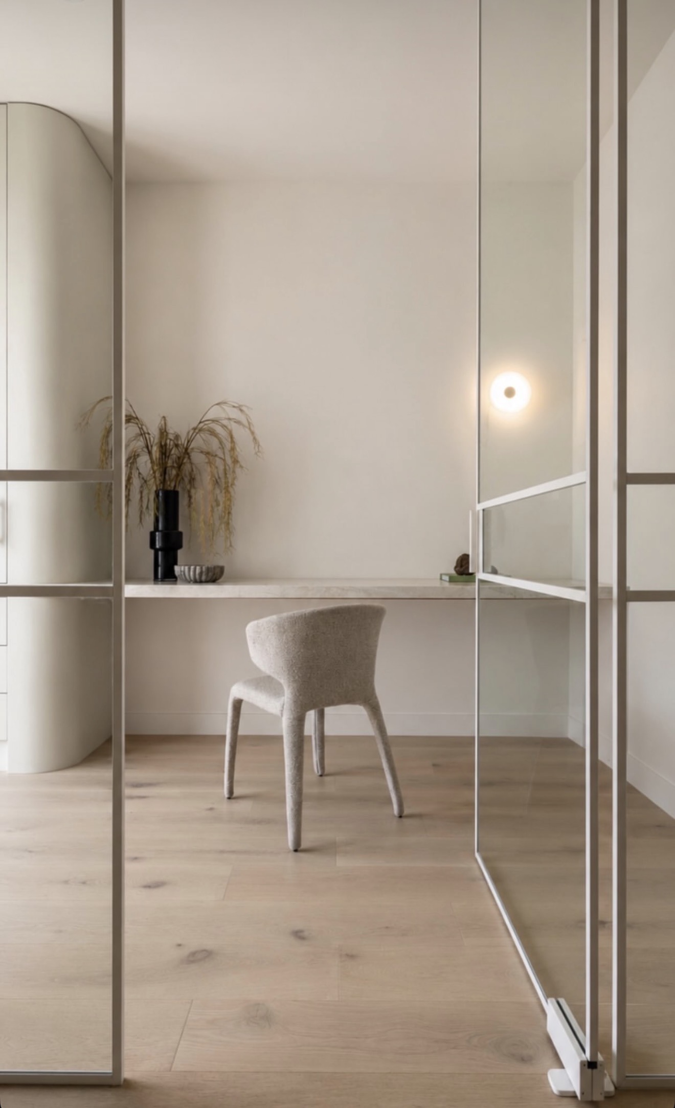 Open white-framed glass office door with a desk and upholstered chair beyond