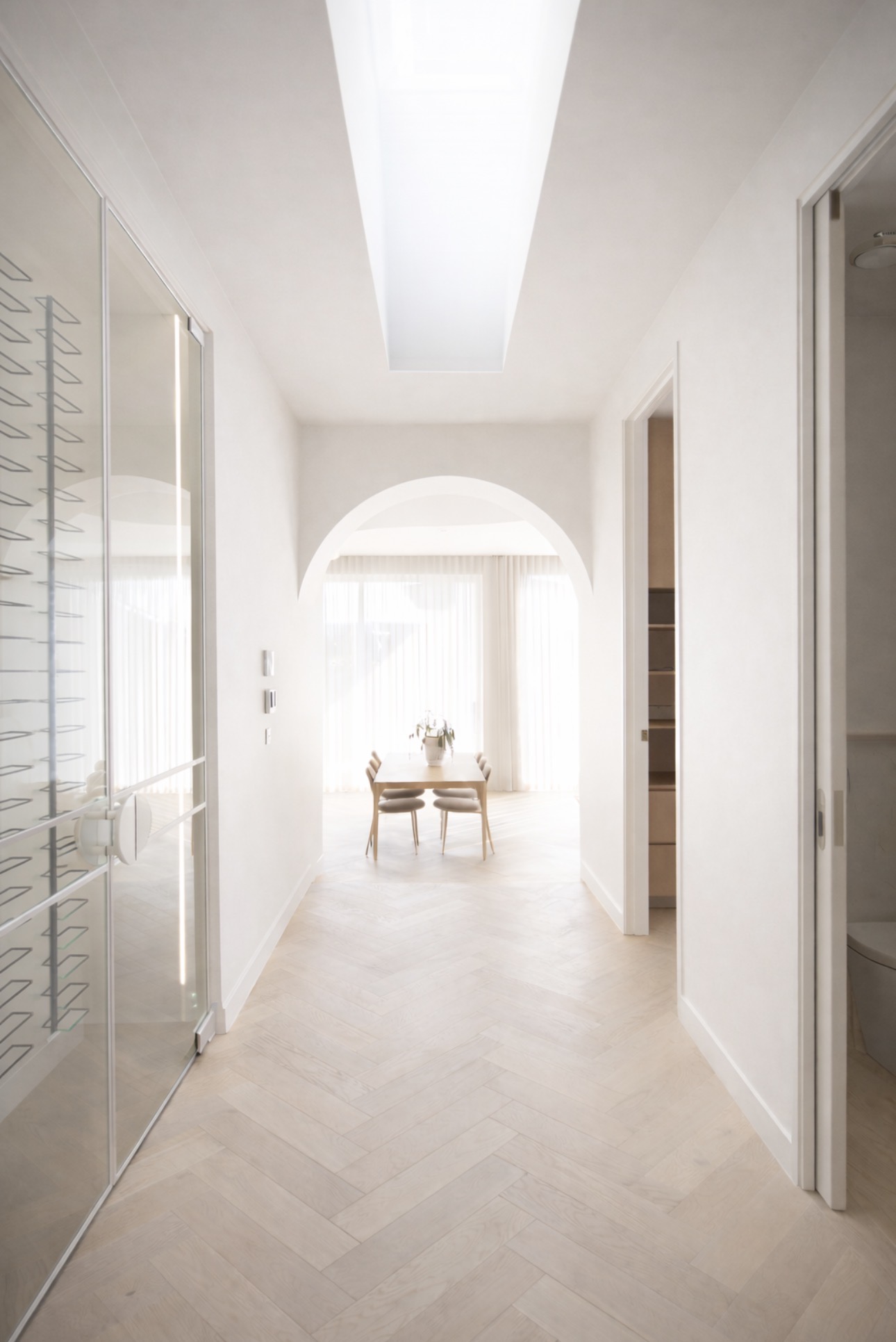 White glass wine-room doors beside a bright hallway with an arched opening