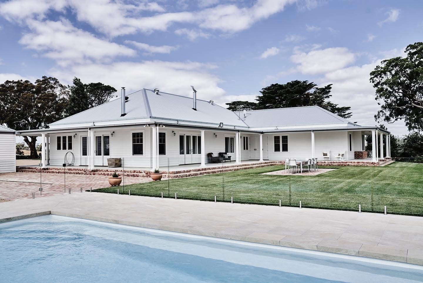 Frameless glass pool fence with a white house and lawn beyond