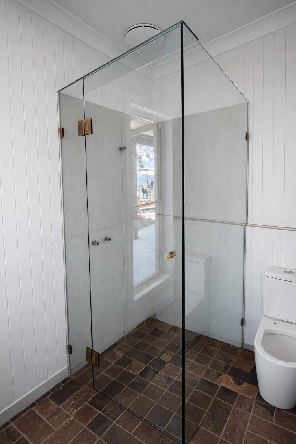 Clear corner shower enclosure with warm metal hardware and brown floor tiles