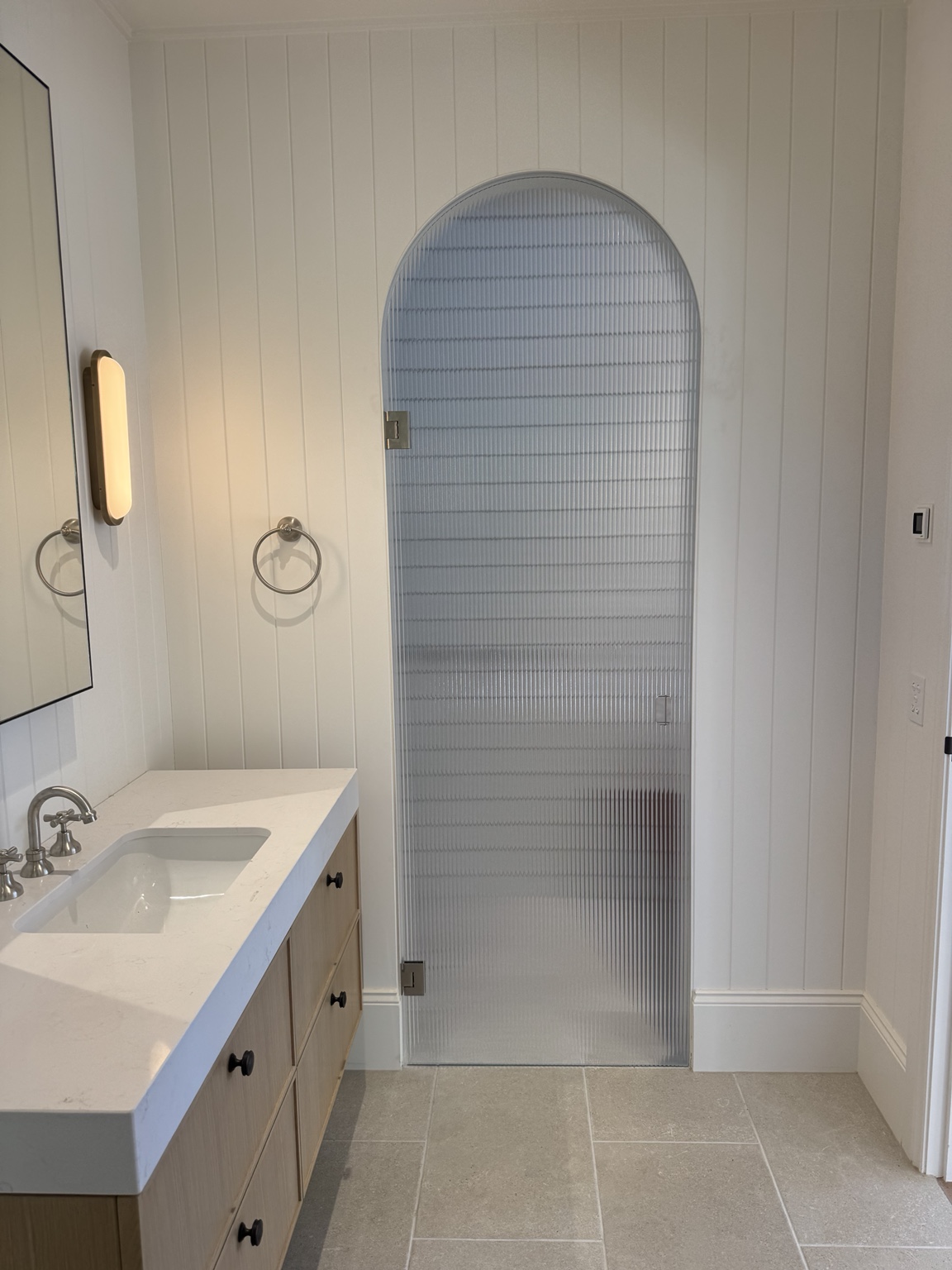 Arched fluted glass shower door beside a timber bathroom vanity