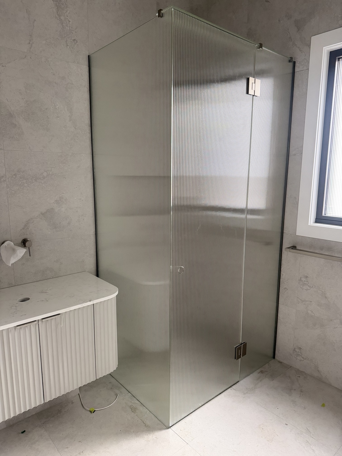 Fluted corner shower enclosure with a hinged door beside a white vanity