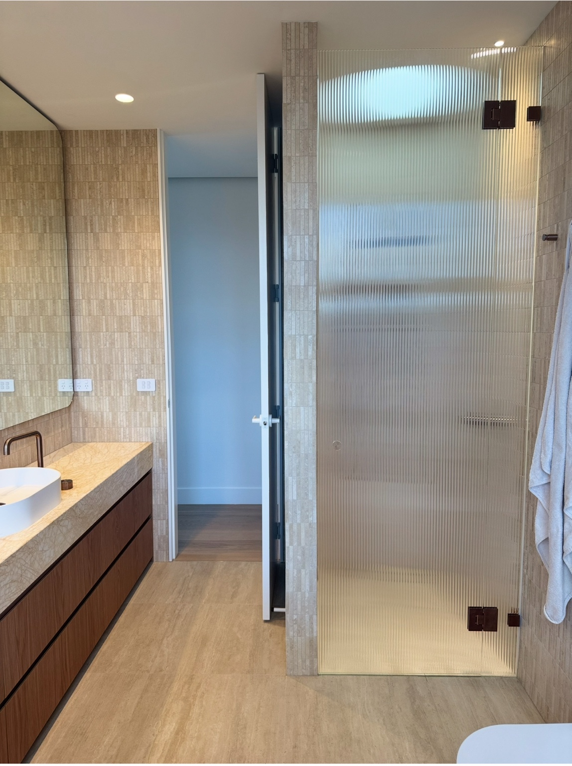 Fluted shower door with dark hardware beside a timber vanity